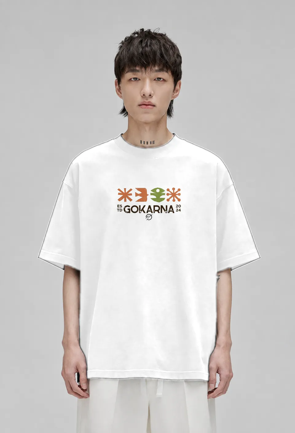 Model wearing the white Gokarna oversized t-shirt with the orange and green Gokarna Estd 2024 print, front view