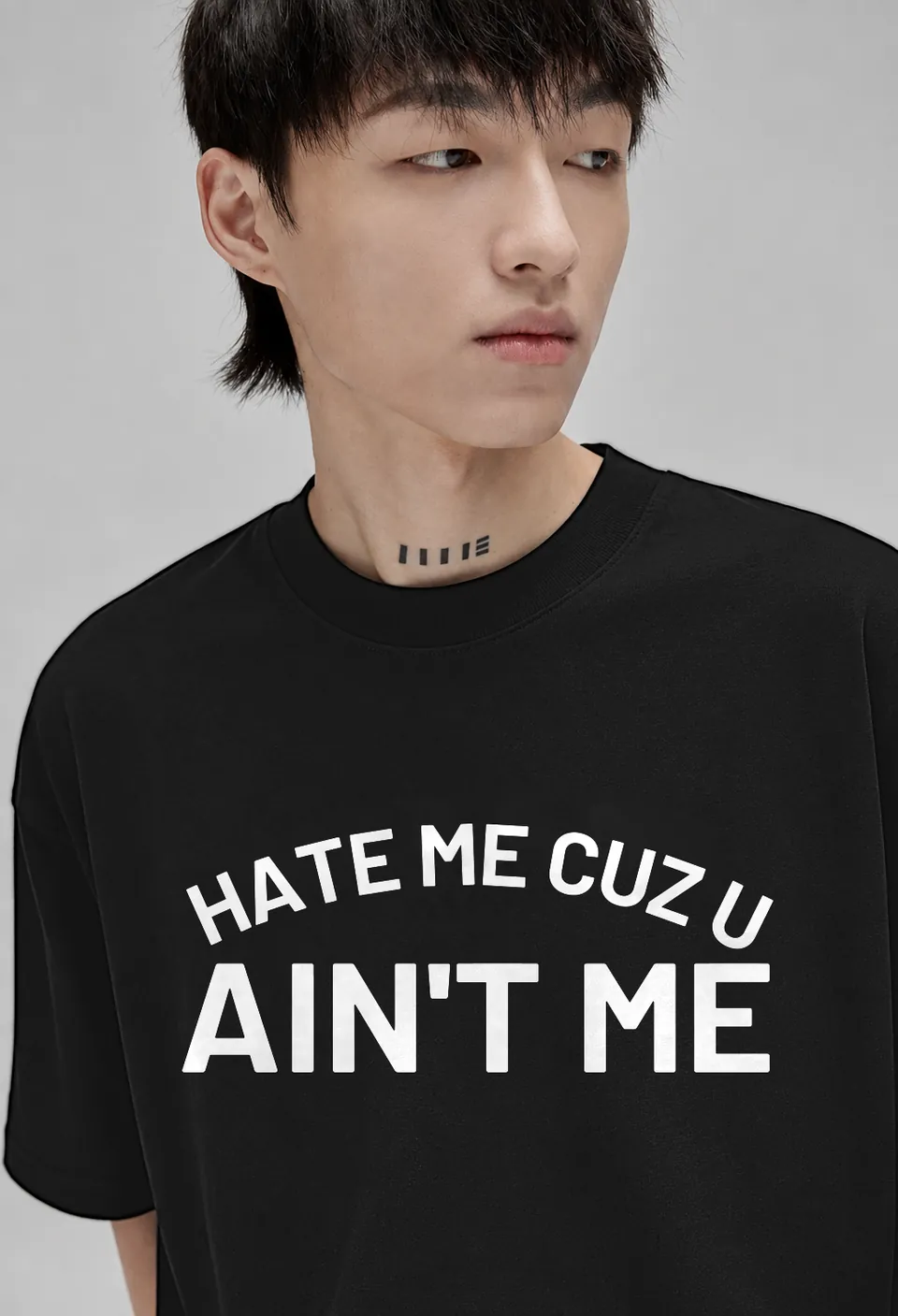 Close-up of the white arched Hate Me Cuz U Ain't Me lettering on a black oversized t-shirt