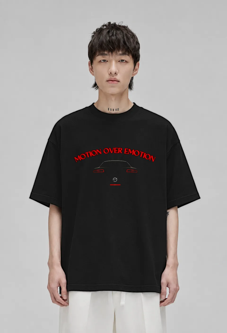 Model wearing the black Motion Over Emotion oversized t-shirt with the red neon Motion Over Emotion arc above a car silhouette with glowing tail lights, front view